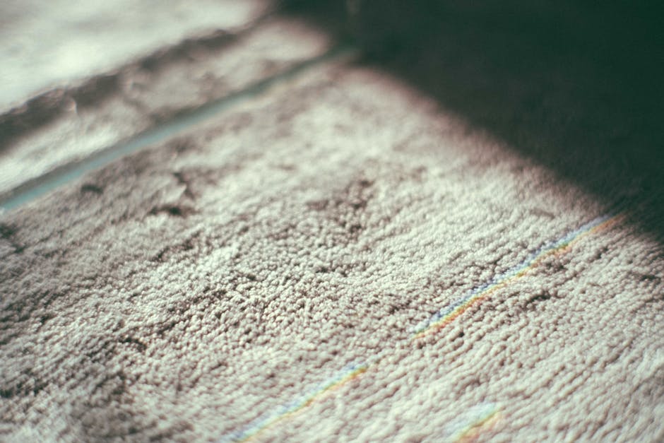 Close-up view of a beige carpet in a residential setting, showing a textured surface with visible fibers. The carpet appears clean and well-maintained, with a slight sheen indicating recent cleaning o